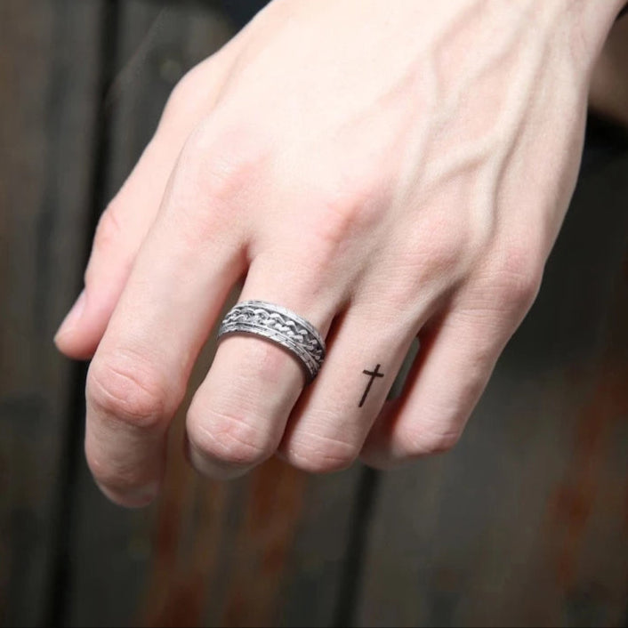 Silberner Herrenring mit Kettenmuster, Kreuz-Tattoo auf Finger, stilvoller Schmuck, Nahaufnahme.
