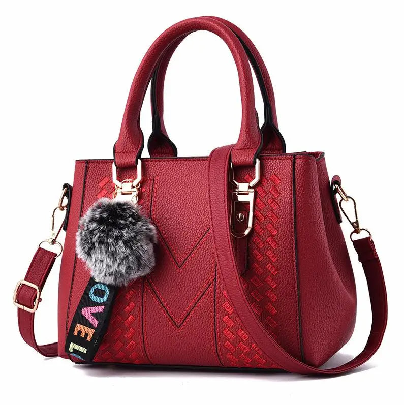 Rote Damenhandtasche aus Leder mit Schulterriemen und Pompon-Anhänger, modisch und elegant.
