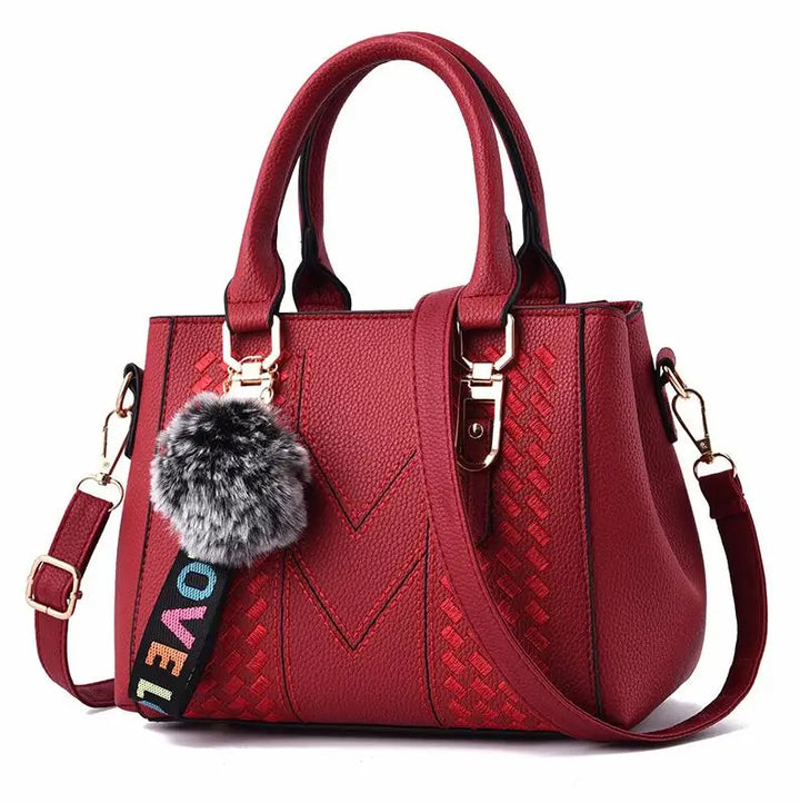Rote Damenhandtasche aus Leder mit Schulterriemen und Pompon-Anhänger, modisch und elegant.