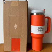 Oranger Thermobecher mit Griff, Edelstahl, 1,1 Liter, neben brauner Verpackung, ideal für unterwegs.