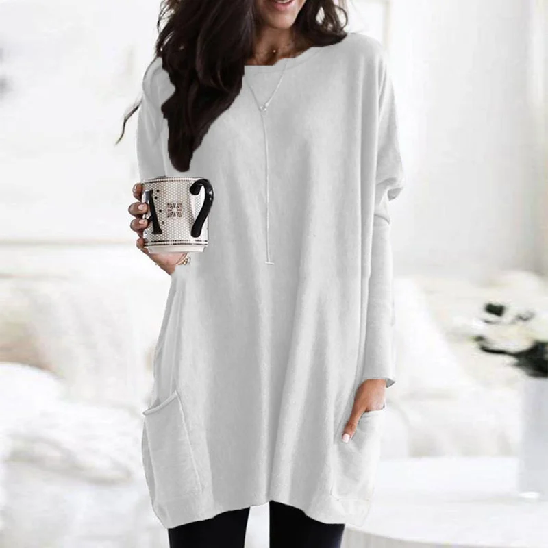 Frau in weißem Oversize-Pullover mit Kaffeetasse, gemütliche Wintermode, Wohnzimmer.