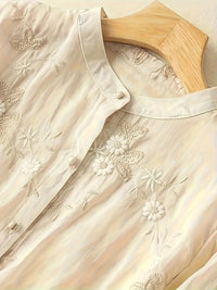 Weiße bestickte Bluse aus Baumwolle auf Holzkleiderbügel, florales Design, Damenmode.