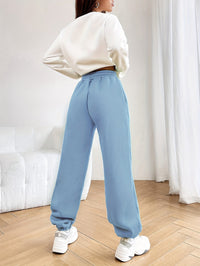 Frau in blauer Jogginghose und weißem Pullover, moderne Freizeitmode, Holzboden, Innenraum.