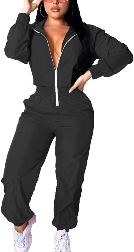 Frau in schwarzem Jumpsuit mit Reißverschluss, Sonnenbrille und weißen Sneakers.