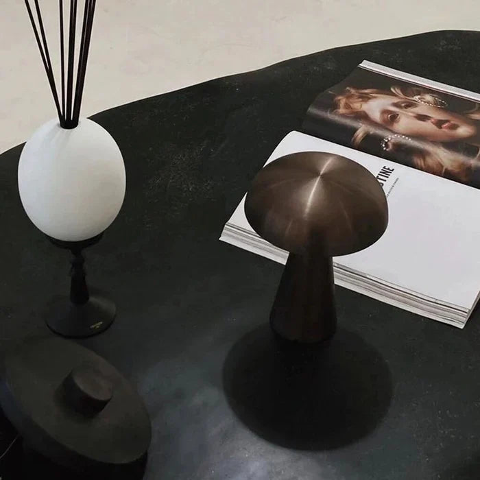 Schwarze Tischlampe aus Metall neben Duftstäbchen und offenem Magazin auf dunklem Tisch.