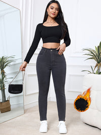 Frau in schwarzem Crop-Top und grauer Jeans, hält schwarze Handtasche, modisch, modern.