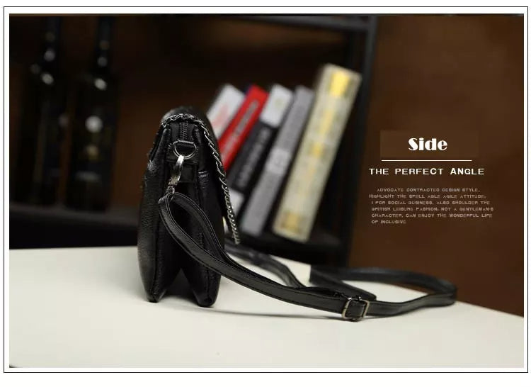 Schwarze Ledertasche mit verstellbarem Riemen, seitliche Ansicht, auf Tisch vor Bücherregal.