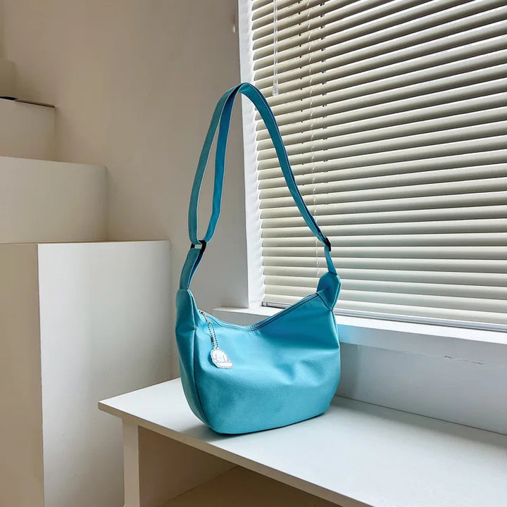 Blaue Umhängetasche aus Stoff auf weißem Tisch, modernes Design, Damenmode Accessoire.