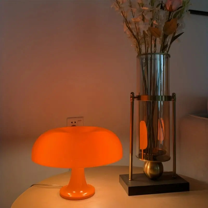 Orangefarbene Pilzlampe auf Tisch neben hoher Vase mit Blumen, moderne Inneneinrichtung, stimmungsvolles Licht.