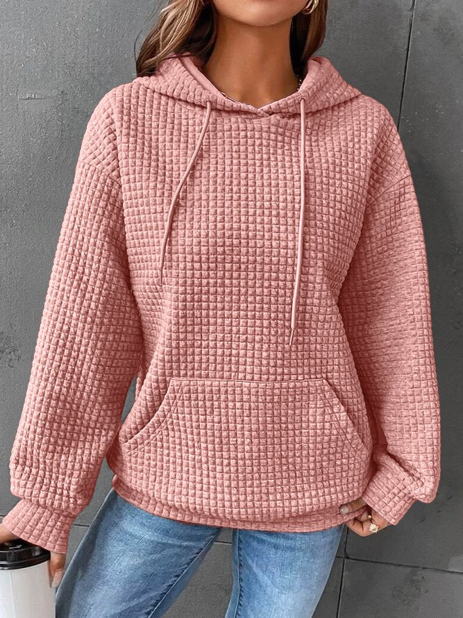 Frau in rosa Kapuzenpullover aus Strickstoff, lässig, mit Kängurutasche, grauer Hintergrund.