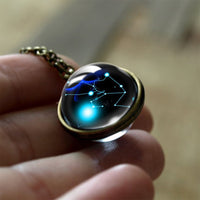 Hand hält bronzefarbenen Anhänger mit leuchtendem Sternbild-Design, Glaskuppel, Schmuck.