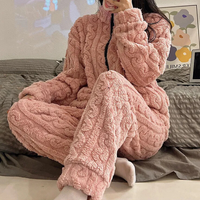 Frau in rosa Plüsch-Pyjama, gemütlich, warm, Winterkleidung, auf grauem Sofa sitzend.