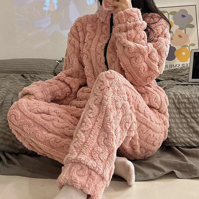 Frau in rosa Plüsch-Pyjama, gemütlich, warm, Winterkleidung, auf grauem Sofa sitzend.