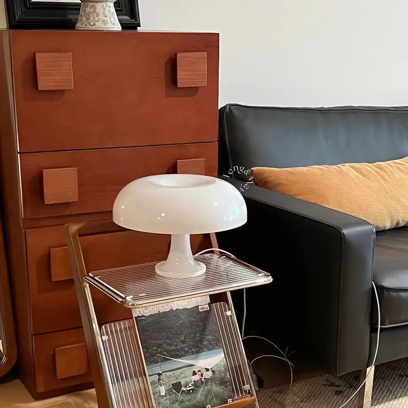 Weiße Tischlampe auf Metallregal neben schwarzem Ledersofa und brauner Kommode im Wohnzimmer.