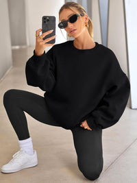 Frau in schwarzem Oversize-Pullover und Leggings, Sonnenbrille, Smartphone, weiße Sneaker.