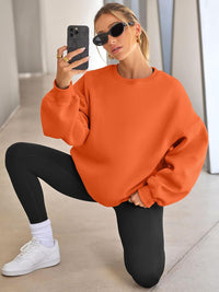 Frau in orangefarbenem Oversize-Pullover, schwarze Leggings, weiße Sneaker, Sonnenbrille, Smartphone.