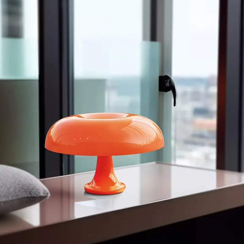 Orangefarbene Pilzlampe aus Glas auf Tisch vor Fenster, modernes Design, Innenbeleuchtung.