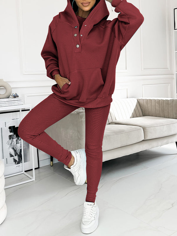 Frau in rotem Hoodie-Set, Kapuze, Knöpfe, weiße Sneakers, modernes Wohnzimmer, Mode-Outfit.
