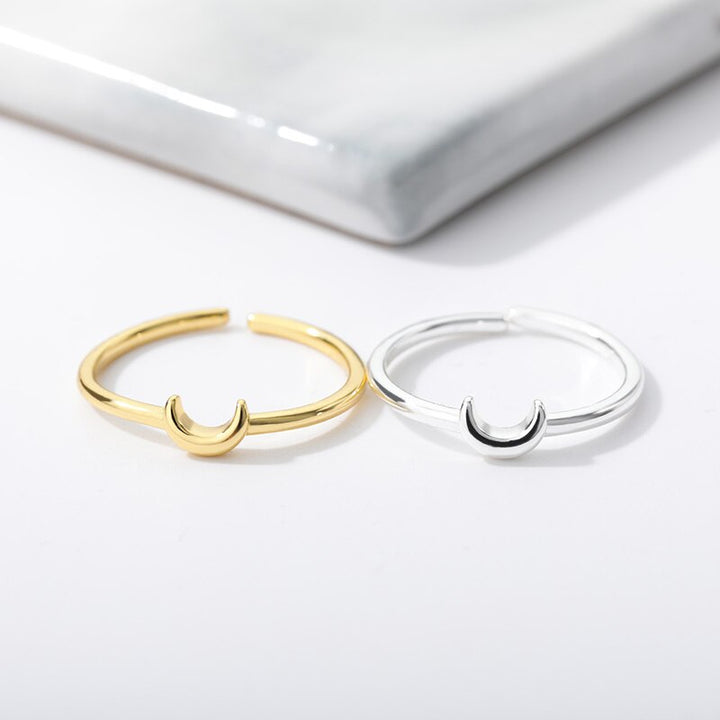 Zwei offene Ringe, gold und silber, mit Halbmond-Design auf weißem Hintergrund.