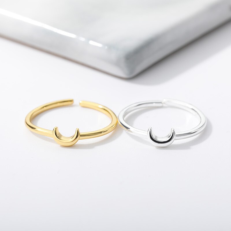 Zwei offene Ringe, gold und silber, mit Halbmond-Design auf weißem Hintergrund.