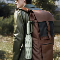 Mann mit brauner Ledertasche und grünem Regenschirm im Freien.