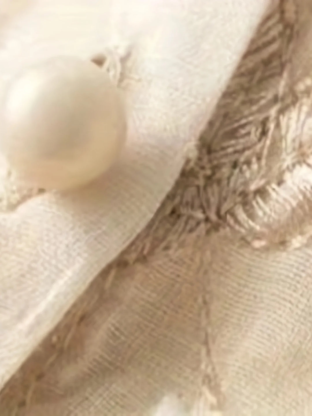 Nahaufnahme einer cremefarbenen Seidenbluse mit Perlenknopf und Stickerei.