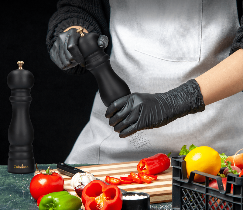 Person mahlt Pfeffer mit schwarzer Pfeffermühle, Gemüse auf Schneidebrett, Küchenszene.