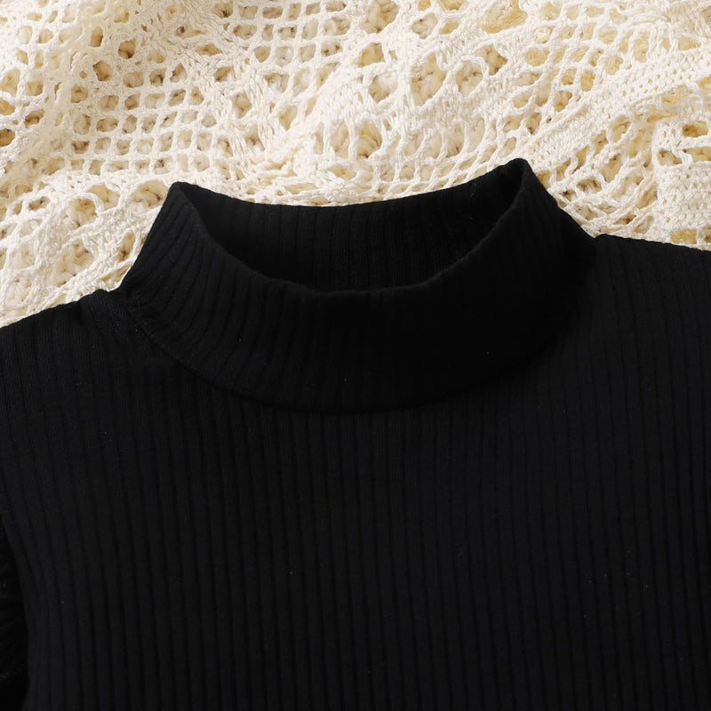 Schwarzer Rollkragenpullover aus Rippstrick auf cremefarbenem Häkelhintergrund.