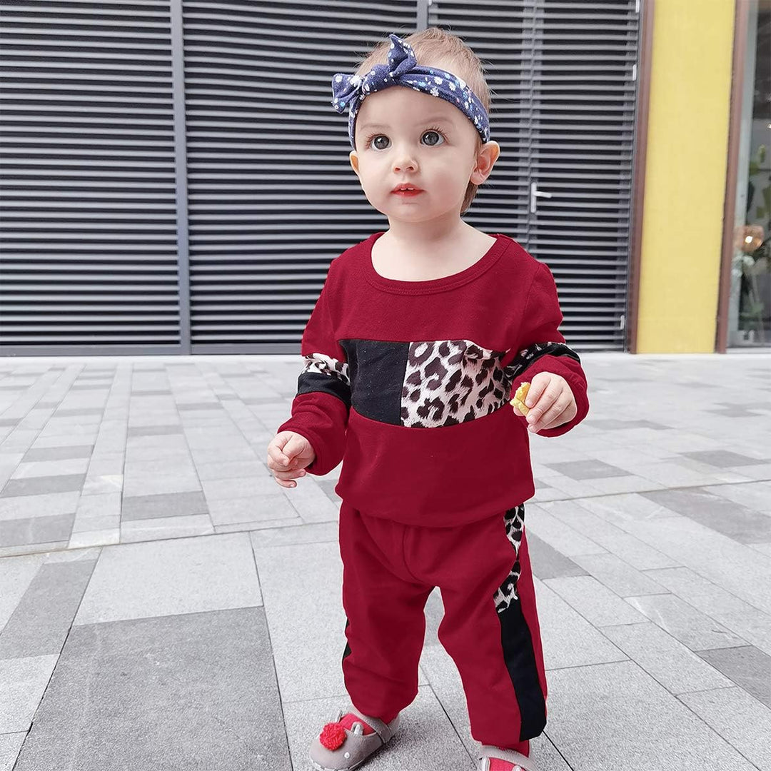 Kleinkind in rotem Leopardenmuster-Outfit mit Stirnband, draußen stehend.