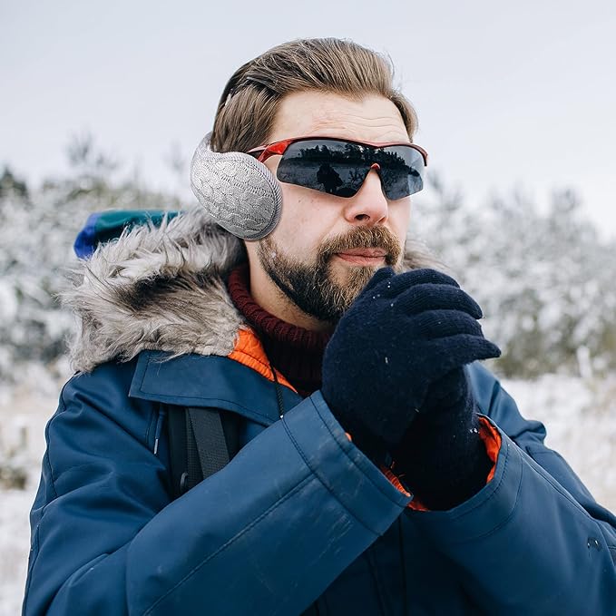 Mann mit blauer Winterjacke, Sonnenbrille und Ohrenschützer im verschneiten Wald.