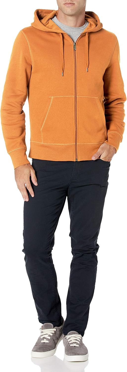 Mann in orange Kapuzenjacke mit Reißverschluss, grauem T-Shirt, schwarzen Hosen und grauen Sneakers.