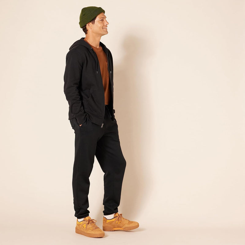 Mann in schwarzem Hoodie und Jogginghose, braune Sneaker, grüner Beanie, lässige Mode.