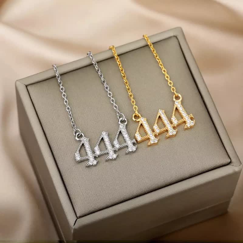 Drei Halsketten mit 444-Anhänger, Silber und Gold, auf beigem Hintergrund.