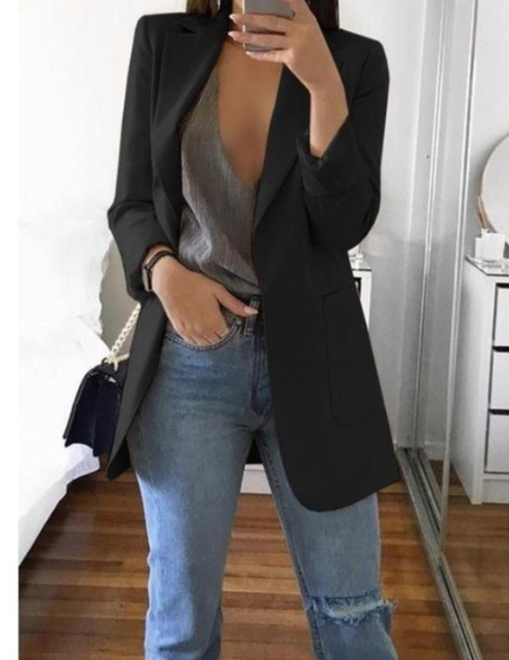 Frau in schwarzem Blazer, grauem Top und Jeans, hält Smartphone, modisch, modern, Spiegel.