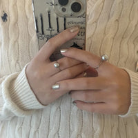 Frau mit Perlenring und Smartphone, beige Strickpullover, modisches Accessoire, Nahaufnahme.