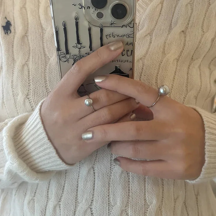 Frau mit Perlenring und Smartphone, beige Strickpullover, modisches Accessoire, Nahaufnahme.