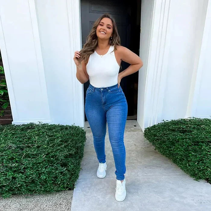 Frau in blauer Jeans und weißem Top vor Haustür, lächelnd, modisch, lässiger Stil.