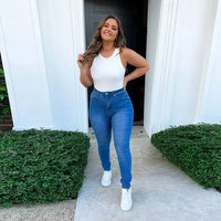 Frau in blauer Jeans und weißem Top vor Haustür, lächelnd, modisch, lässiger Stil.