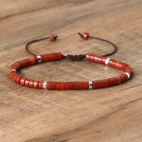 Rotes Perlenarmband aus Holz mit silbernen Akzenten auf Holztisch, verstellbar, handgefertigt.