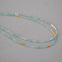 Türkisfarbene Perlenkette mit goldenen Akzenten auf grauem Hintergrund, Schmuckdesign.