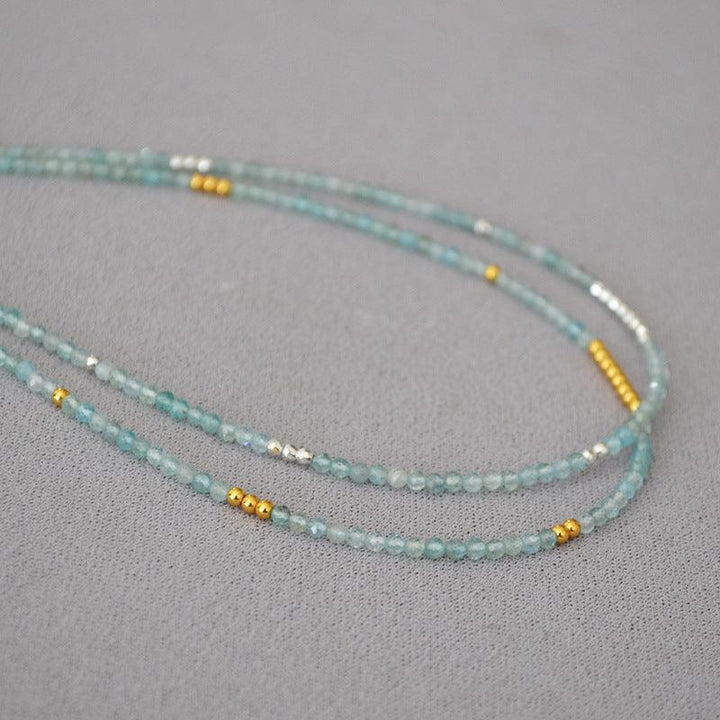 Türkisfarbene Perlenkette mit goldenen Akzenten auf grauem Hintergrund, Schmuckdesign.