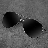 Schwarze Aviator-Sonnenbrille mit Metallrahmen auf grauem Hintergrund.