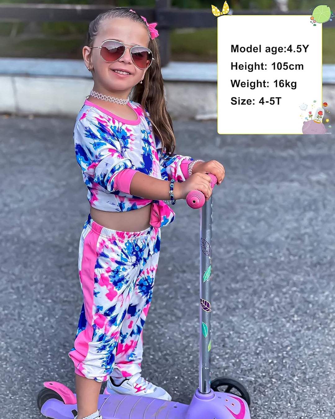 Mädchen in buntem Freizeitanzug mit Roller, Sonnenbrille, lächelnd, draußen.