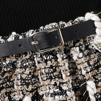 Schwarzer Ledergürtel mit silberner Schnalle auf gemustertem Stoffrock, modisches Accessoire.