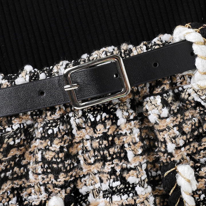 Schwarzer Ledergürtel mit silberner Schnalle auf gemustertem Stoffrock, modisches Accessoire.