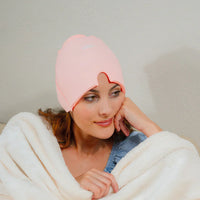 Frau mit rosa Wärmekappe, gemütlich unter weißer Decke, Haarpflege, Entspannung.