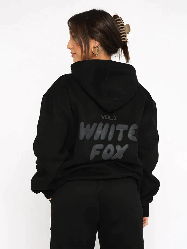 Frau in schwarzem Hoodie mit "White Fox" Aufdruck, Kapuze, lässiger Stil, Streetwear-Mode.