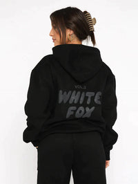 Frau in schwarzem Hoodie mit "White Fox" Aufdruck, Kapuze, lässiger Stil, Streetwear-Mode.