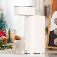 Weißer automatischer Getränkespender auf Küchentheke, Weihnachtsdekoration im Hintergrund.