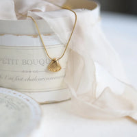 Goldene Muschelkette auf cremefarbener Box, eleganter Schmuck, Damenaccessoire, Geschenkidee.